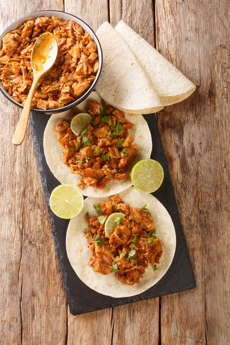 Chilorio is a pork dish from the Mexican state of Sinaloa served with tortilla and lime closeup in the slate board. Vertical top view